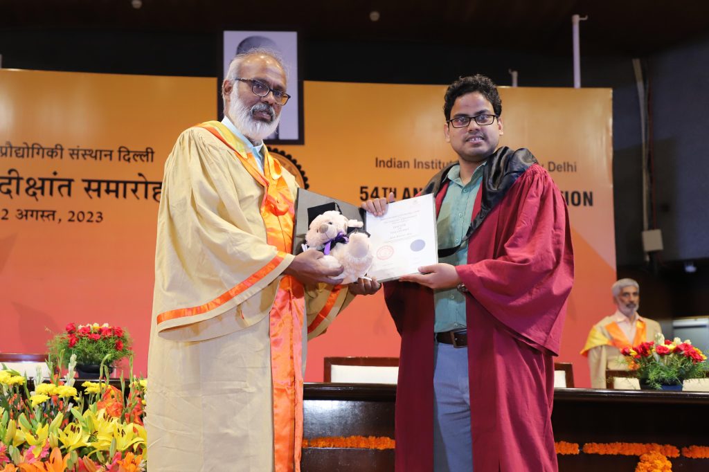 Dr Alok Kumar Ray holding PhD degree on stage with red robes and colourful orange flowers